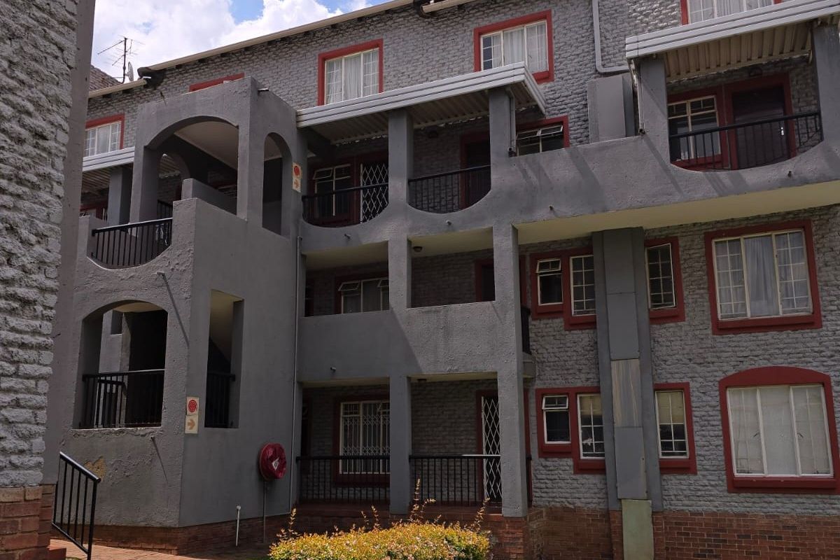 Exterior view of a multi-story apartment complex featuring grey brick facade, private balconies, and landscaped garden areas.