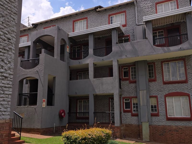 Exterior view of a multi-story apartment complex featuring grey brick facade, private balconies, and landscaped garden areas.