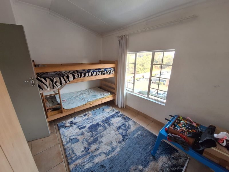 A functional bedroom featuring tiled flooring, a large window providing natural light, and a built-in cupboard for storage.