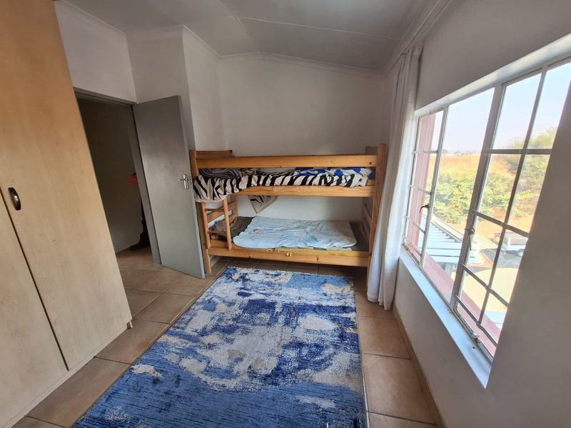 A functional bedroom featuring tiled flooring, a built-in wardrobe, and a large window providing natural light.