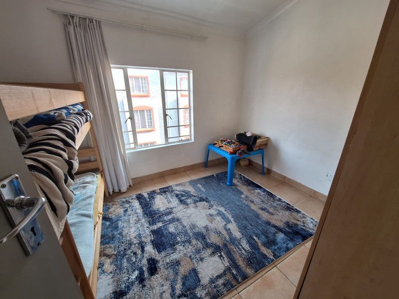 A standard bedroom featuring tiled flooring and a window with a curtain rail, providing a functional space for residents.