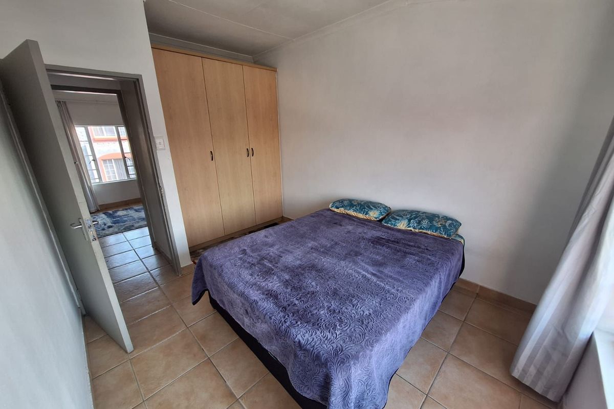 A bedroom featuring built-in wooden wardrobes, tiled flooring, and a coved ceiling, with an adjacent hallway visible through the doorway.