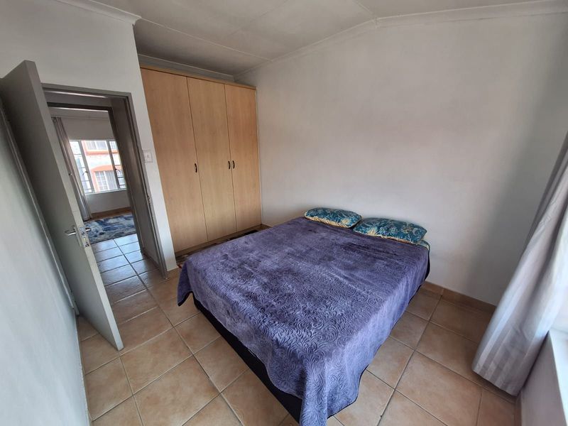 A bedroom featuring built-in wooden wardrobes, tiled flooring, and a coved ceiling, with an adjacent hallway visible through the doorway.