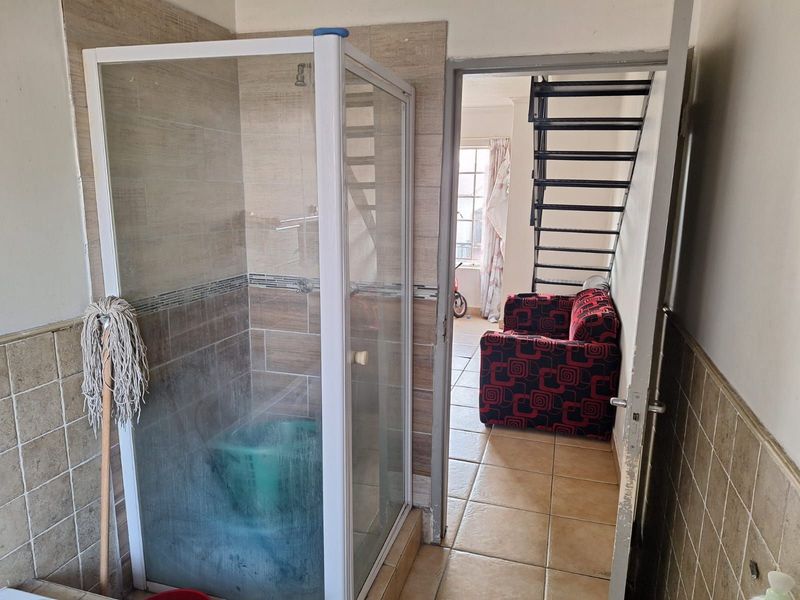 A bathroom featuring a shower enclosure with tiled walls and flooring, with an adjacent view into a living area containing a metal staircase.