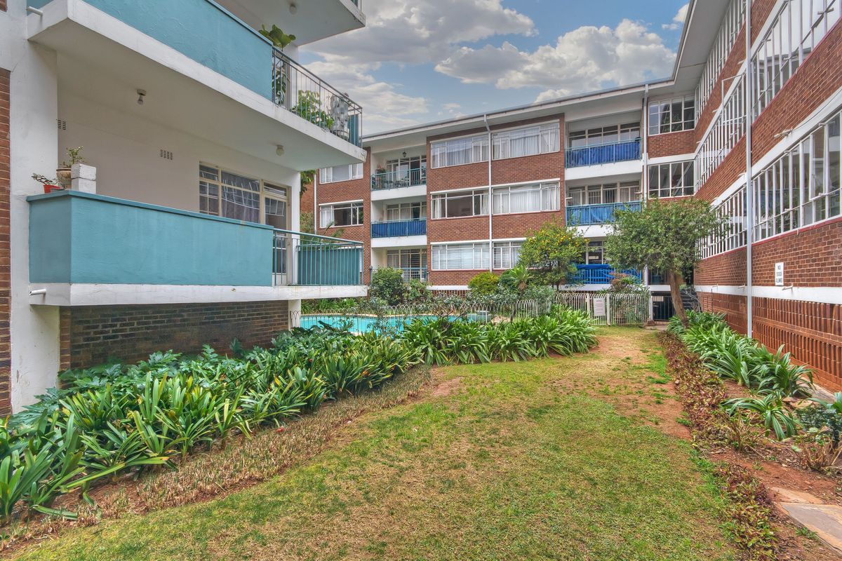 A view of the apartment complex courtyard featuring a communal swimming pool, landscaped garden areas, and private balconies.