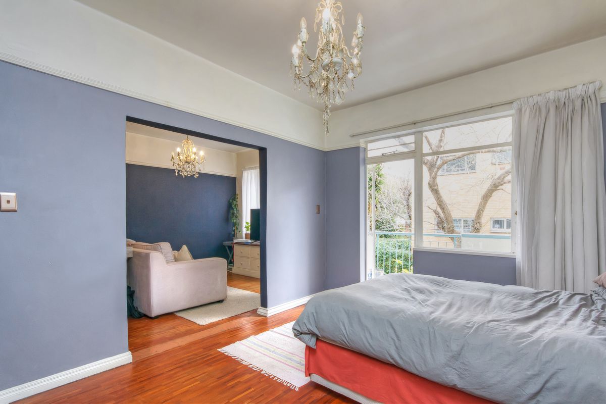 Spacious bedroom featuring polished timber floors, high ceilings with crown molding, and direct access to a private balcony through large windows.