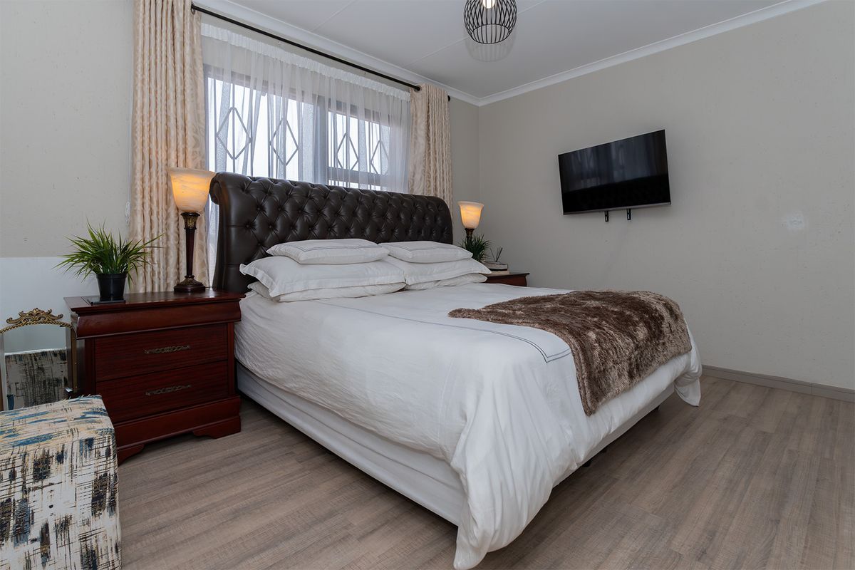 A well-maintained bedroom featuring light wood-look flooring, a window with security bars, and a wall-mounted television.