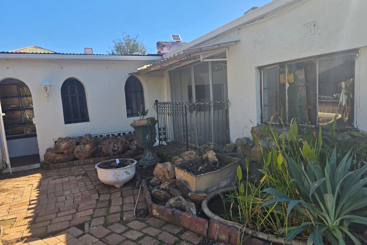 Rear exterior view of the property featuring a brick paved patio area, arched windows, and metal security gates.