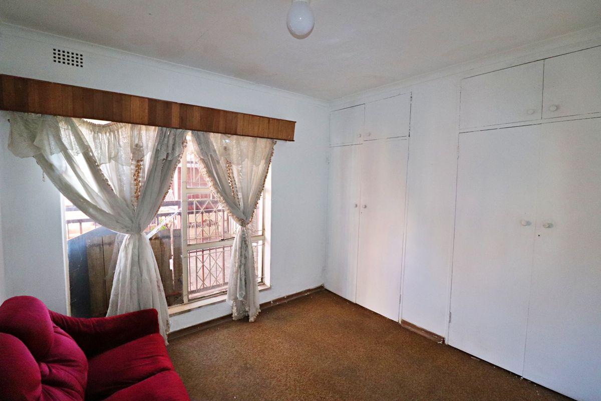 A bedroom featuring built-in storage cupboards, a large window with wooden pelmet, and carpeted flooring.