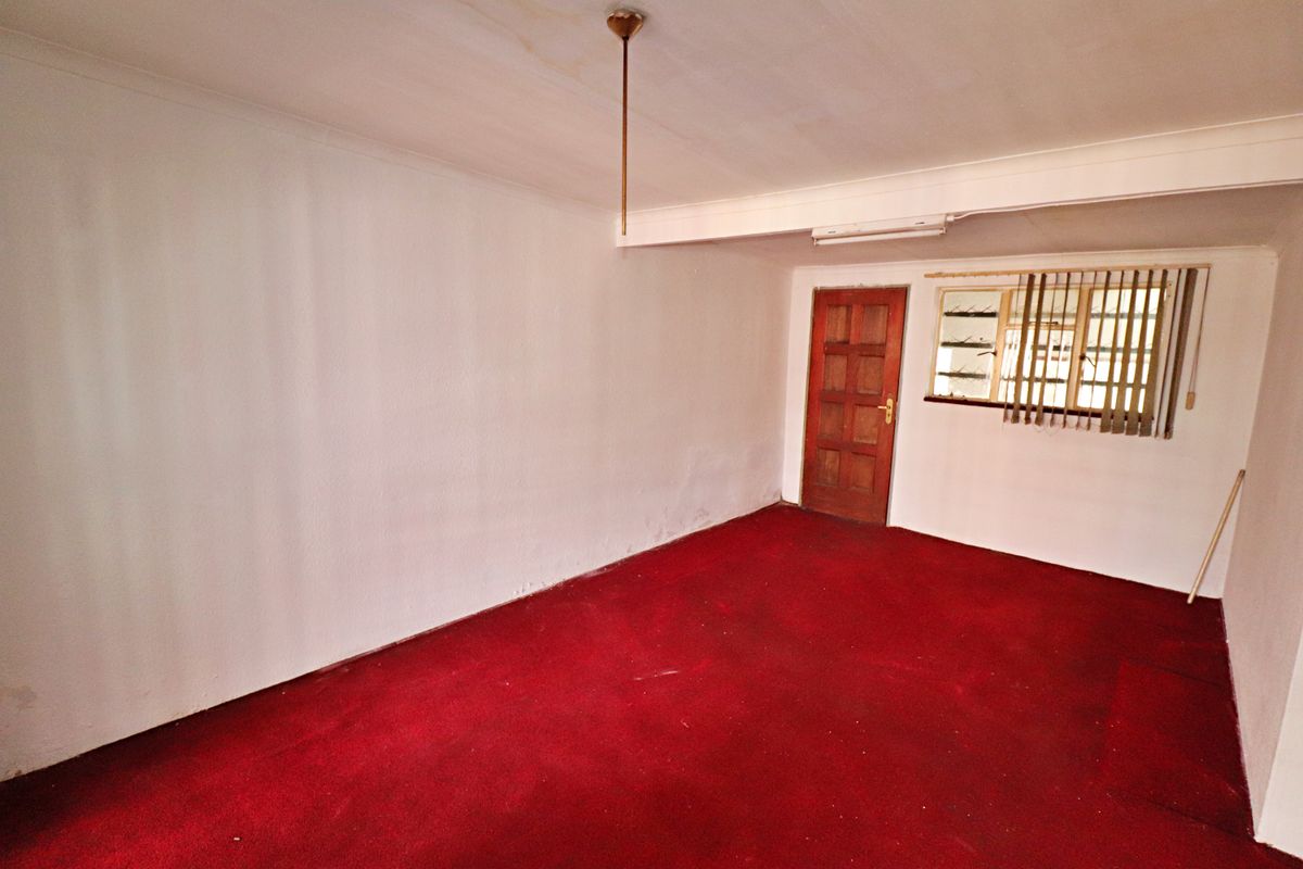An empty living room featuring red carpeting, a wooden door, and a window with fitted blinds.