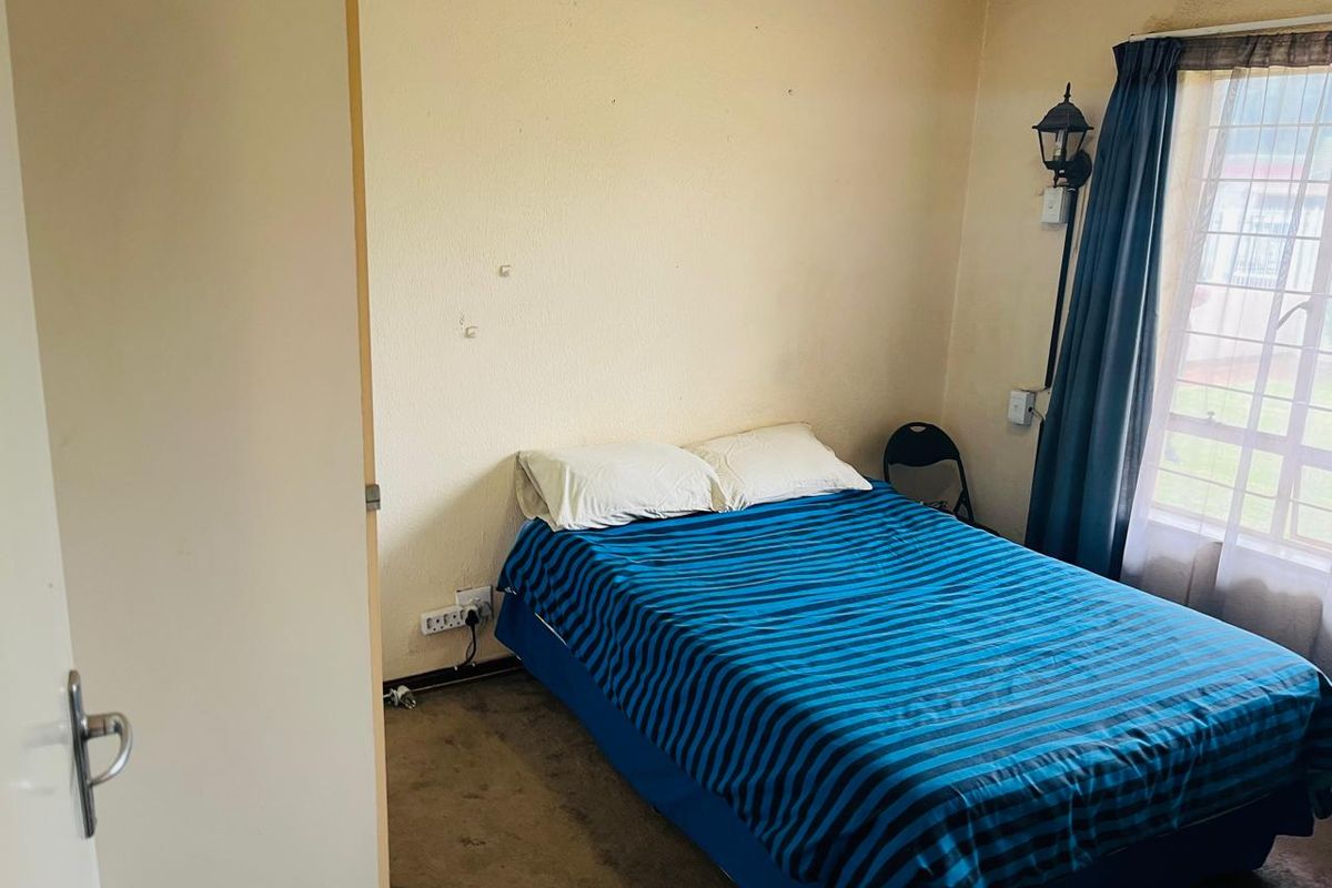 A bedroom featuring a window with curtains, wall-mounted lighting, and electrical outlets, requiring cosmetic updates to the walls and flooring.