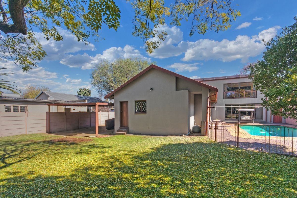 Rear view of the property featuring a swimming pool, paved patio area, and a covered outdoor structure set within a private garden.