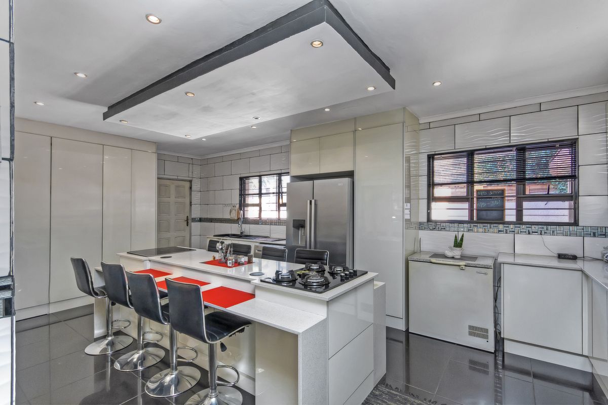 Modern kitchen featuring a large central island with dual hobs, high-gloss cabinetry, integrated appliances, and recessed ceiling lighting.
