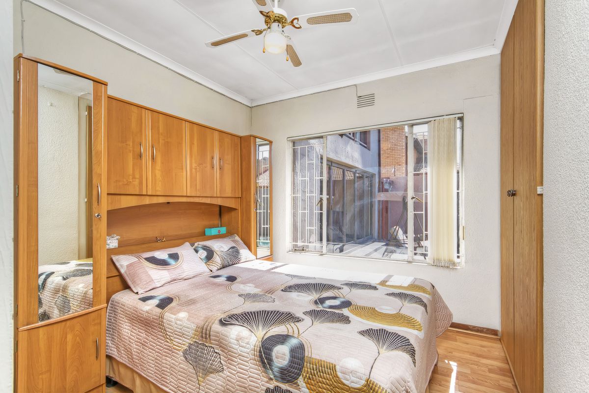 A bedroom featuring built-in wooden cabinetry, laminate flooring, and a ceiling fan, with security bars installed on the window.