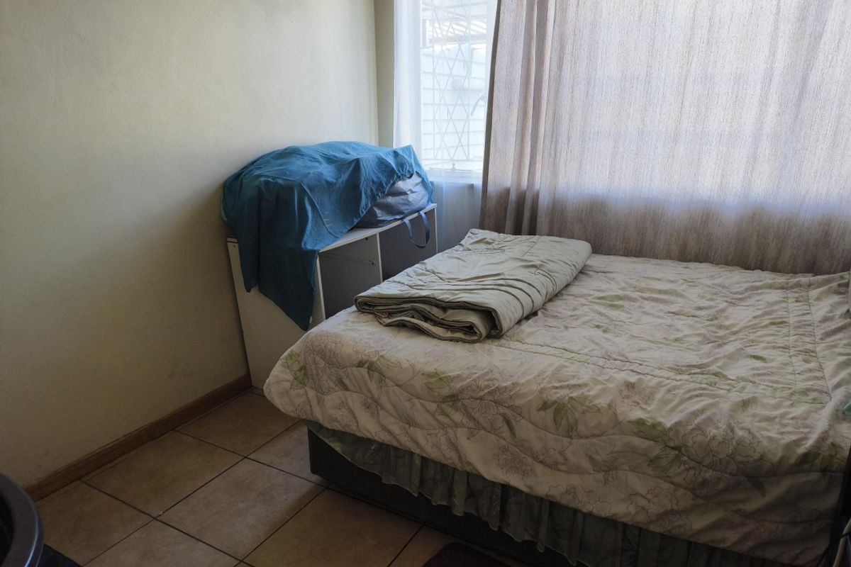 A bedroom featuring tiled flooring and a large window with curtains, providing natural light to the space.