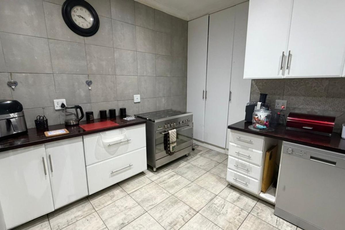 A functional kitchen featuring white cabinetry, dark countertops, tiled flooring, and a stainless steel freestanding oven with extractor fan.