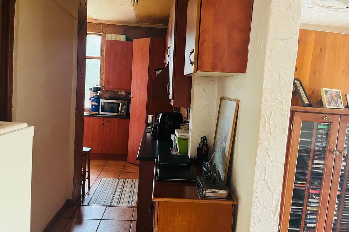 A dated kitchen featuring wood-tone cabinetry, tiled flooring, and a narrow layout, offering potential for a modern renovation.