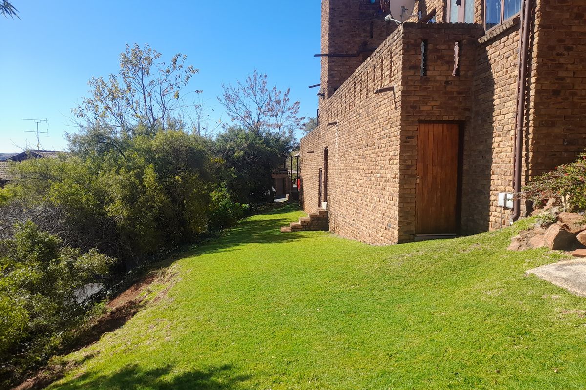A view of the rear exterior of the townhouse, featuring exposed brick facade, a wooden door, and a sloped lawn area.