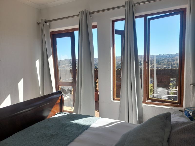A bright bedroom featuring timber-framed windows and a glass door providing access to an outdoor balcony with scenic views.