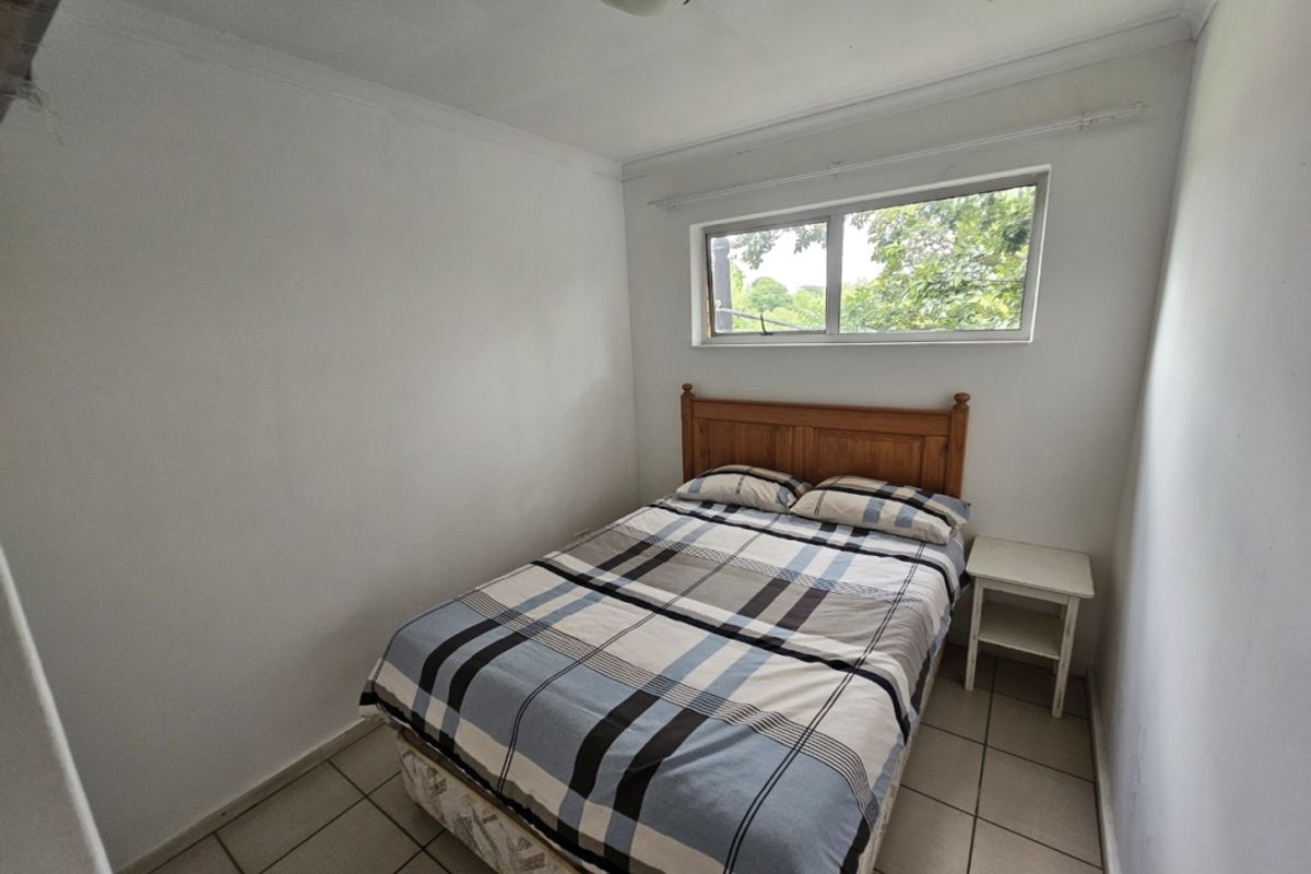 A compact bedroom featuring tiled flooring, a horizontal window, and a simple ceiling-mounted light fixture.
