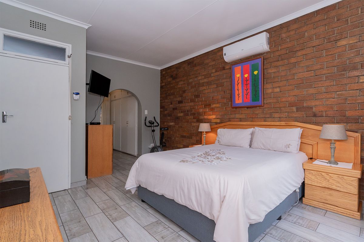Spacious bedroom featuring an exposed brick feature wall, tiled flooring, and a wall-mounted air conditioning unit.