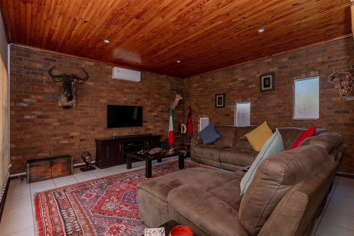 A living room featuring exposed brick walls, a timber-clad ceiling with recessed lighting, and tiled flooring, equipped with a wall-mounted air conditioning unit.