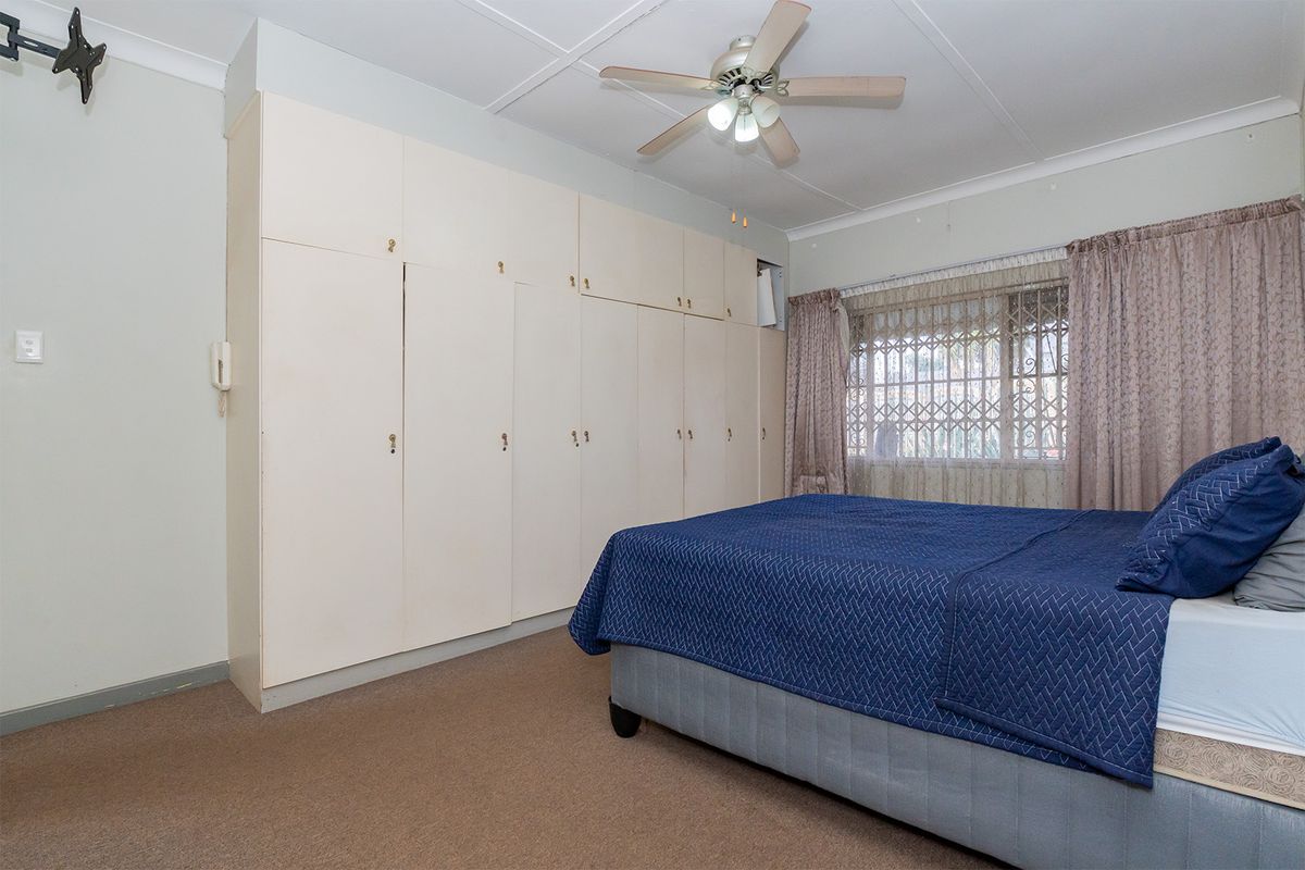 A bedroom featuring built-in floor-to-ceiling cabinetry, a ceiling fan, and security bars on the window.