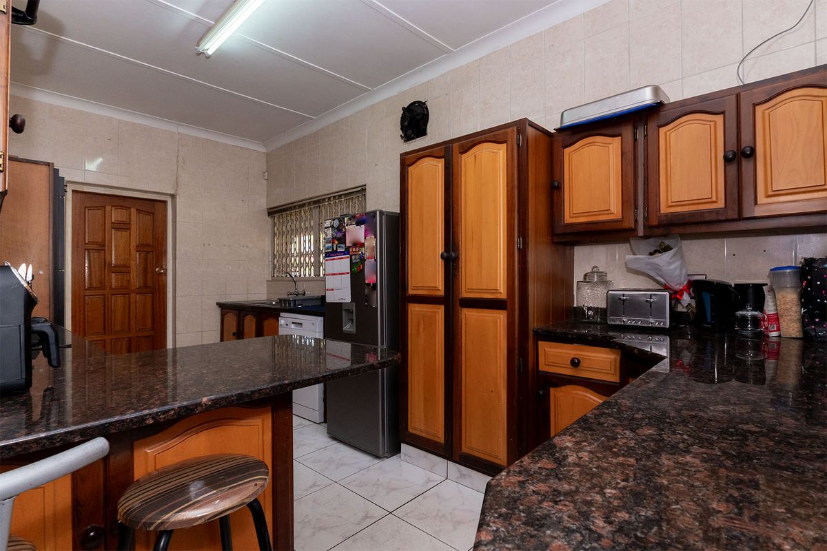 A functional kitchen featuring dark granite countertops, two-tone wooden cabinetry, tiled walls, and a breakfast bar area.