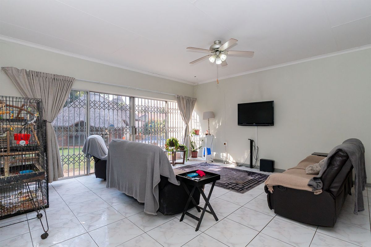 Spacious living room featuring tiled flooring, a ceiling fan, and large sliding glass doors with security gates leading to the outdoor area.