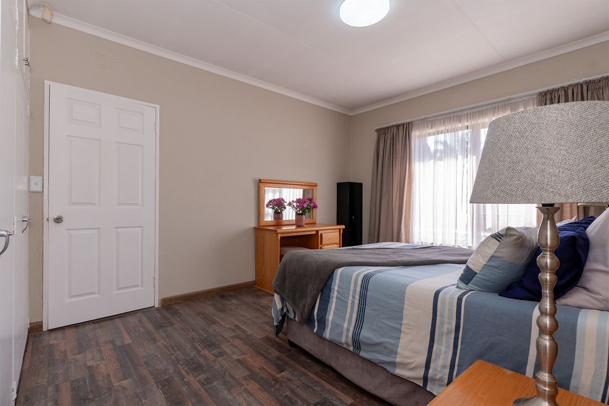 A well-lit bedroom featuring wood-look laminate flooring, neutral wall finishes, and a large window with curtain tracks.