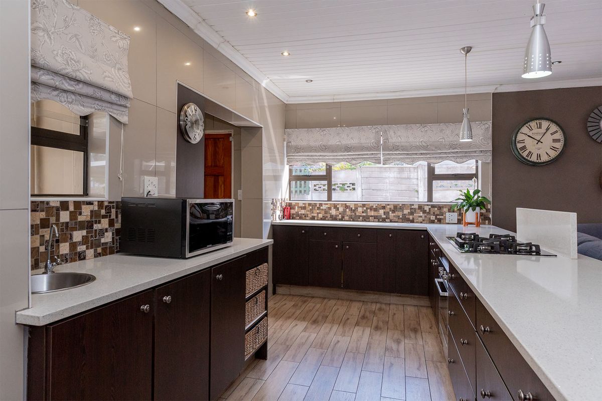 Modern kitchen featuring dark cabinetry, stone countertops, mosaic tile backsplash, integrated gas hob, and wood-look tile flooring.