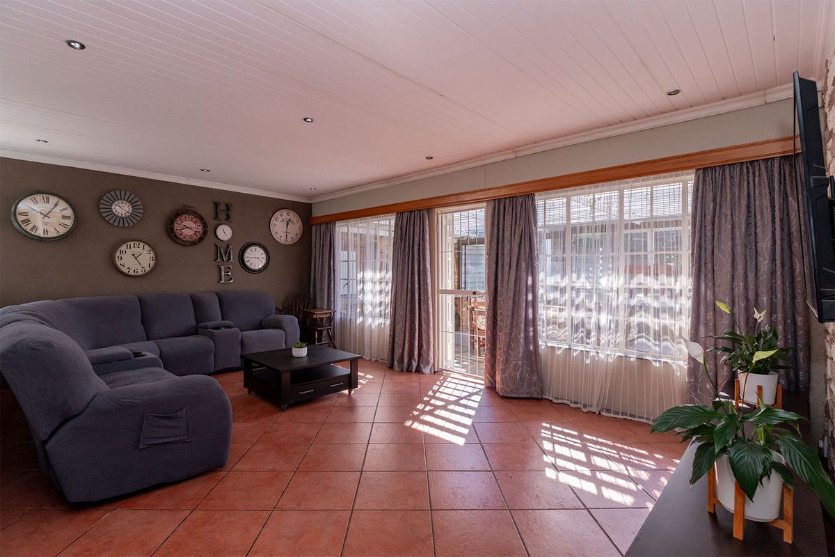 A spacious living room featuring terracotta floor tiles, a white panelled ceiling with recessed lighting, and large windows with access to an outdoor area.