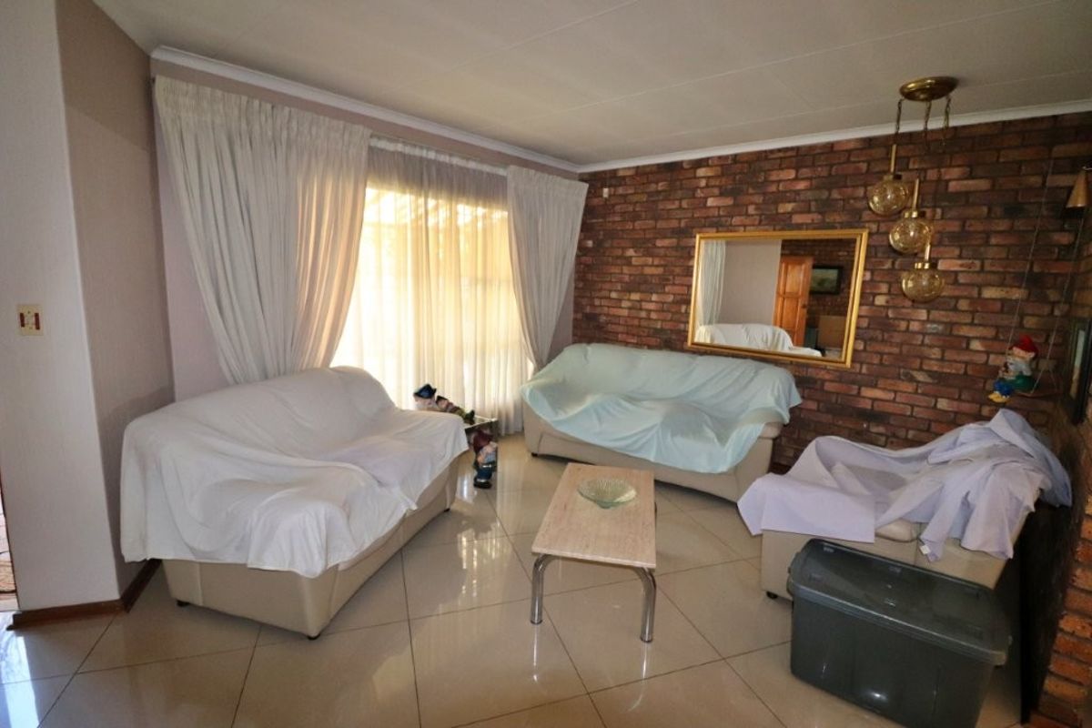 A living room featuring a prominent exposed brick feature wall, tiled flooring, and large windows with curtains.