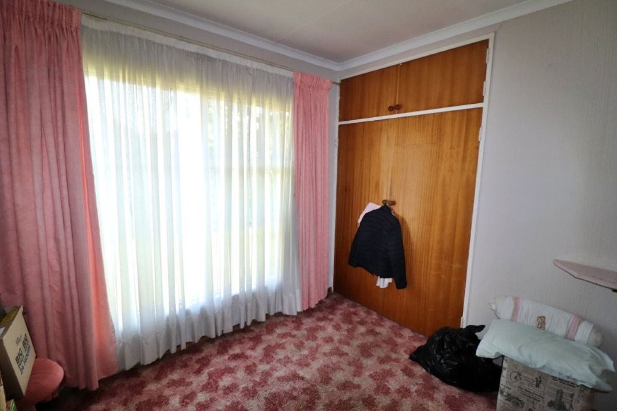 A bedroom featuring built-in wooden cupboards, patterned carpeting, and large windows with curtains.