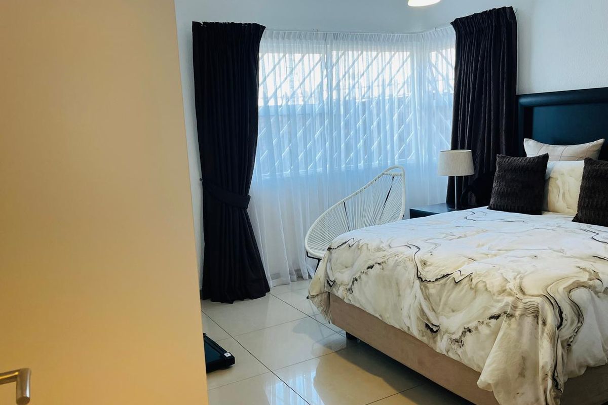 A well-lit bedroom featuring large bay windows with curtains, tiled flooring, and a neutral color palette.