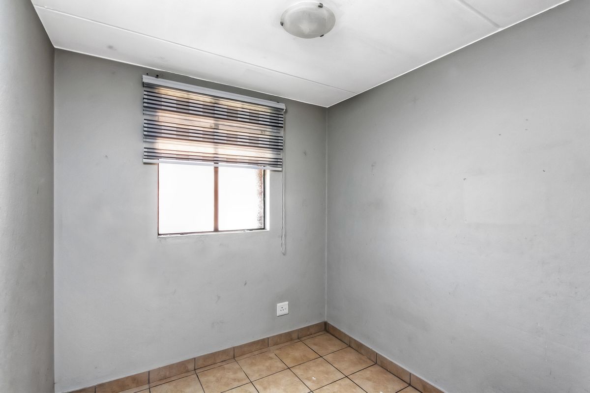 A small, empty bedroom featuring tiled flooring, a single window with a fitted blind, and a central ceiling light fixture.