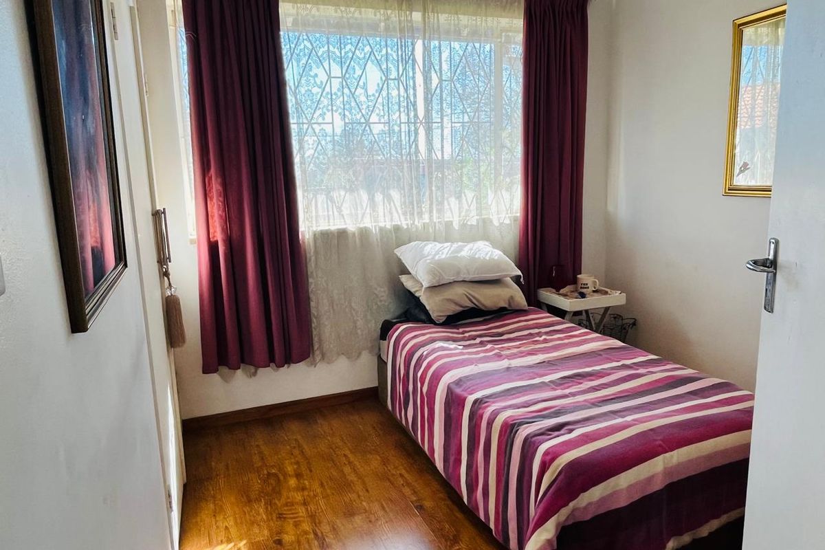 A compact bedroom featuring timber-look flooring, a large window with security bars, and neutral wall finishes.