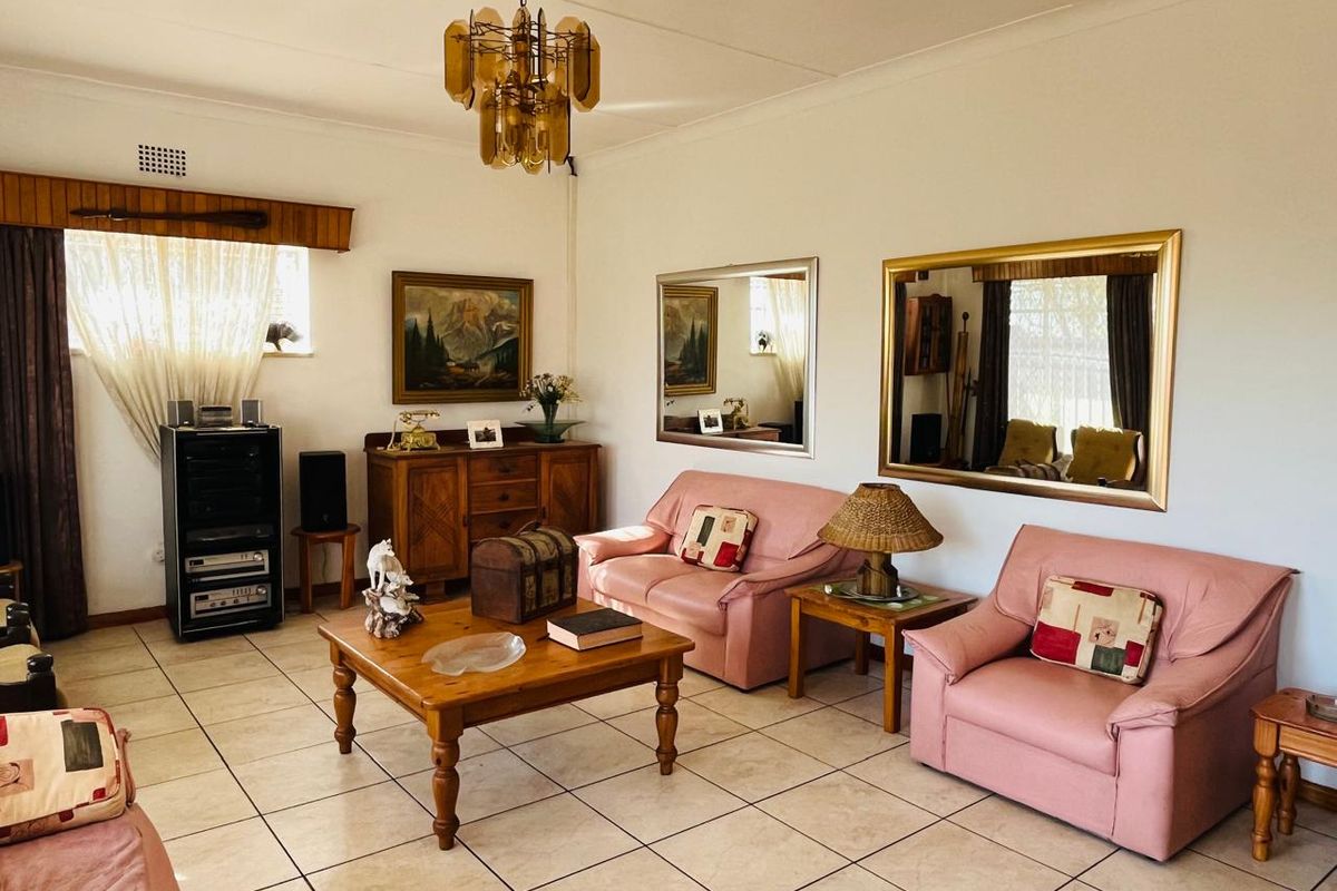 A spacious living room featuring neutral floor tiles, a decorative ceiling light fixture, and large wall-mounted mirrors.