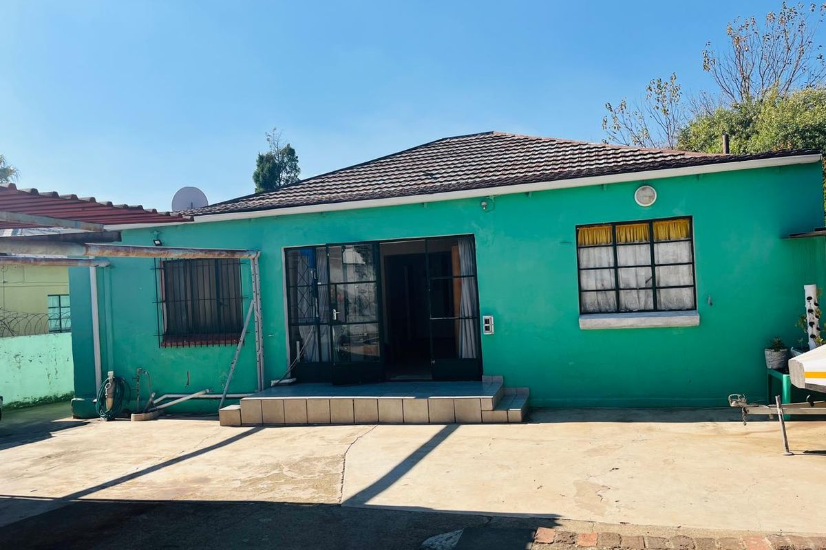 Rear exterior view of the house featuring a tiled patio area, concrete paving, and metal security bars on windows.