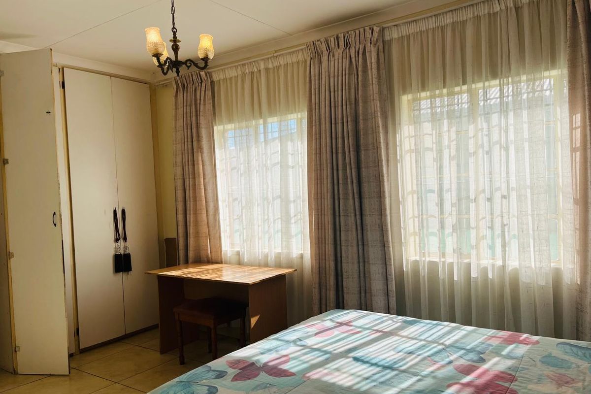 A bedroom featuring built-in cupboards, tiled flooring, and large windows with natural light.