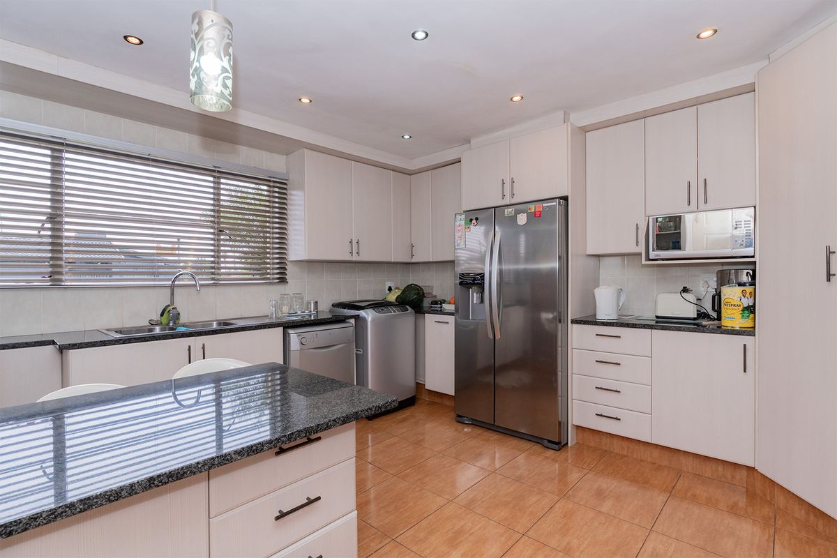 A well-maintained kitchen featuring light-toned cabinetry, granite countertops, tiled flooring, and integrated appliances, offering a functional and clean workspace.