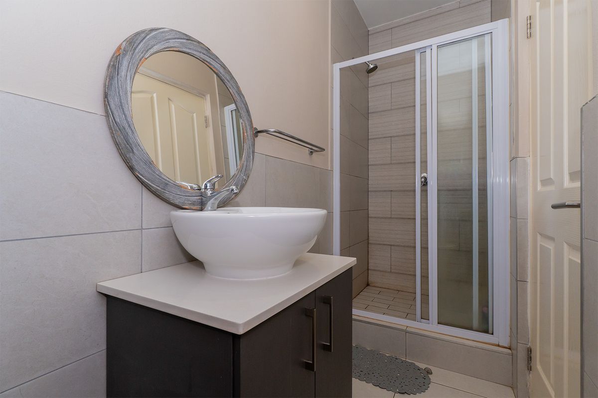 A modern bathroom featuring a vessel sink vanity, a tiled shower enclosure with a glass door, and neutral wall tiling.