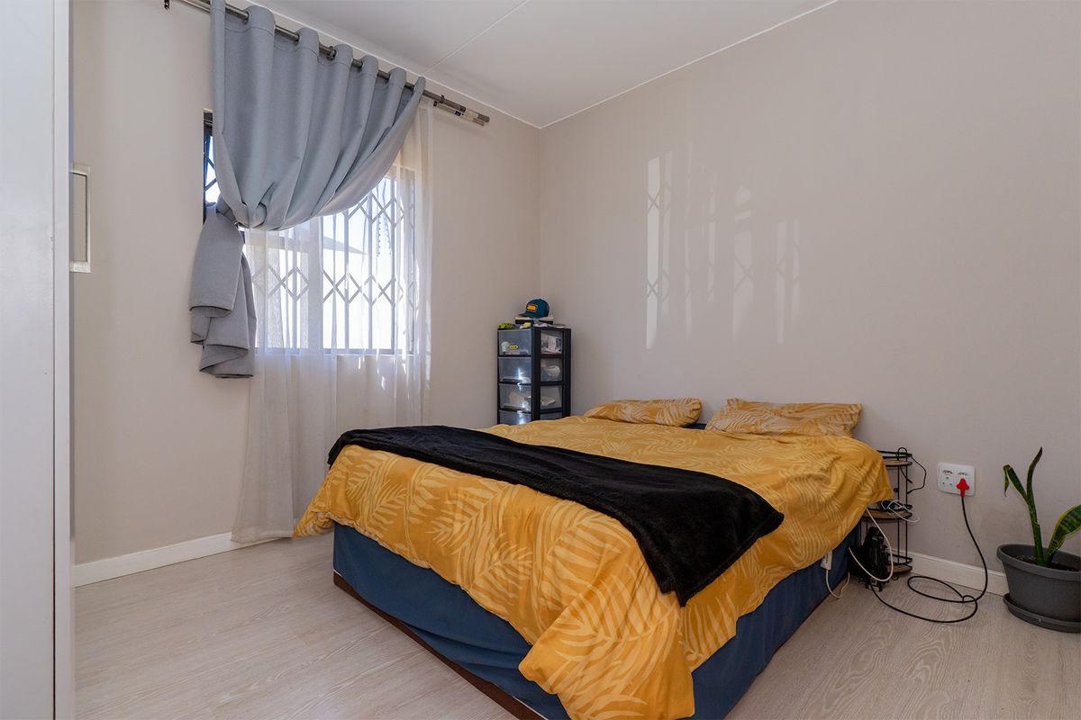 A well-lit bedroom featuring light-toned laminate flooring, neutral wall finishes, and a window secured with a metal security gate.