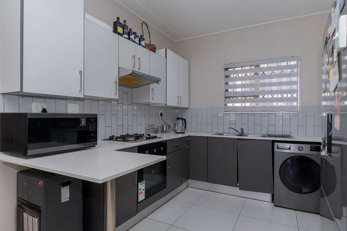 Modern kitchen featuring white upper cabinetry, dark lower cabinets, subway tile backsplash, built-in oven, gas hob, extractor fan, and integrated laundry appliance space.