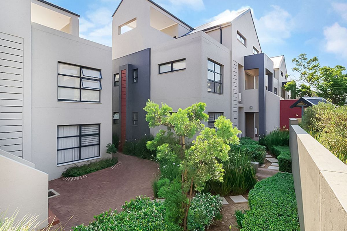 A modern apartment complex exterior featuring contemporary architectural design, paved walkways, and well-maintained landscaped garden areas.