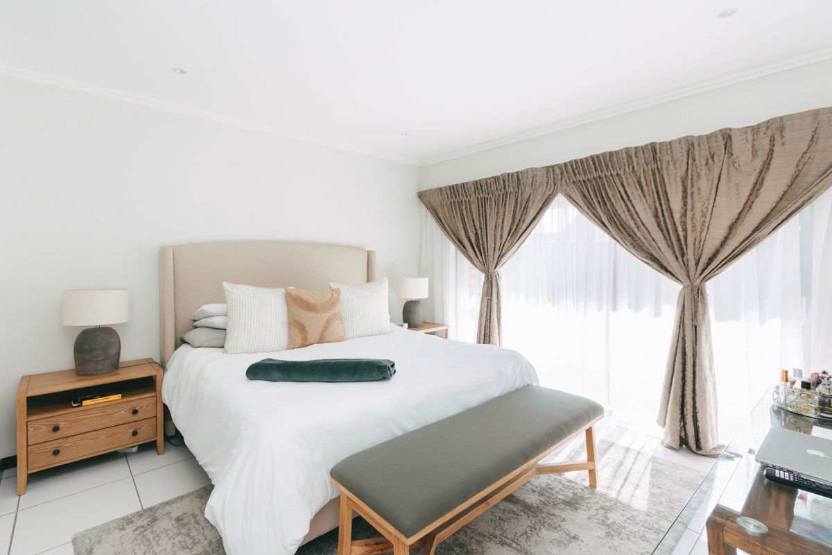 A bright and well-maintained bedroom featuring tiled flooring, recessed ceiling lighting, and large sliding glass doors with curtains providing natural light.