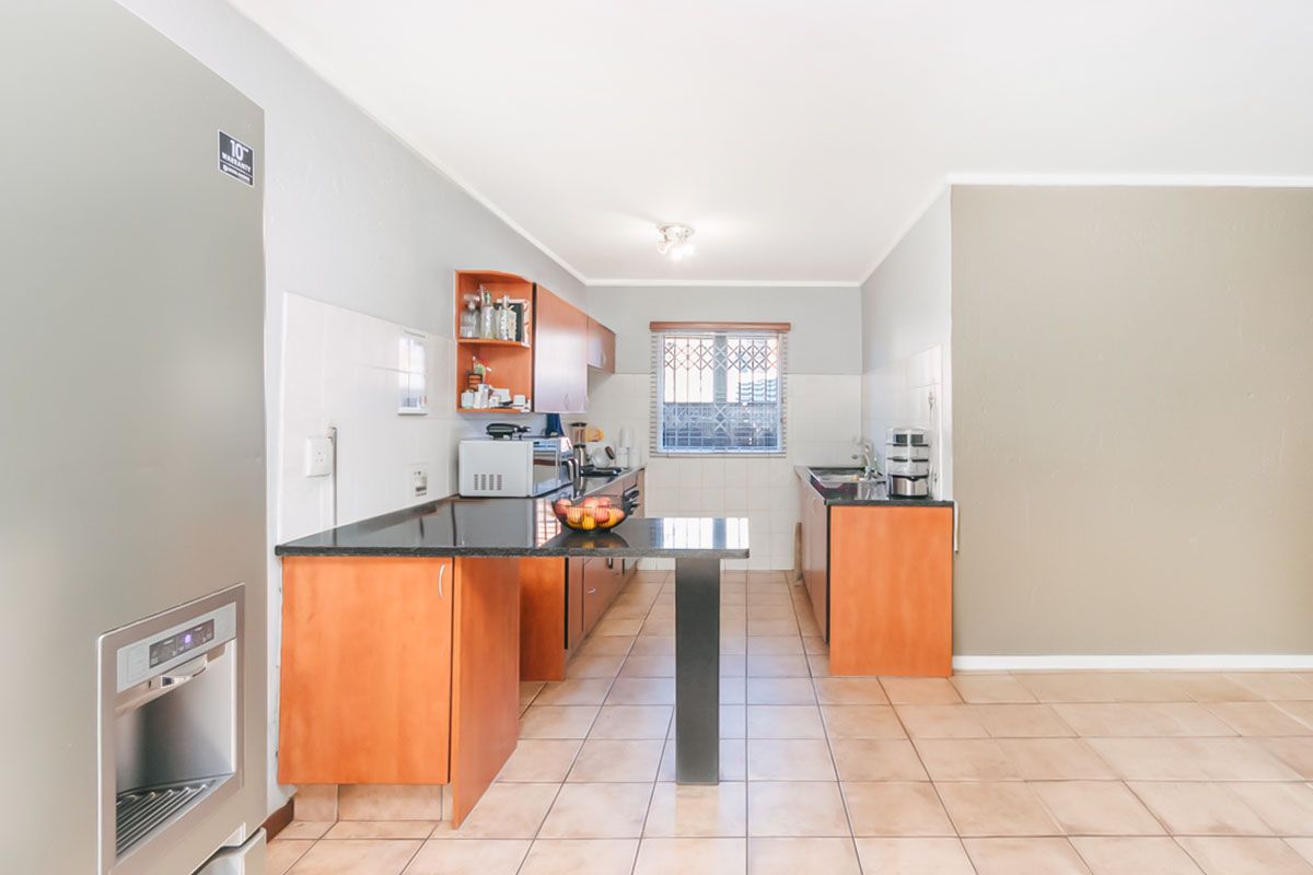 A functional kitchen featuring wooden cabinetry, dark granite countertops, tiled flooring, and a security gate on the window.