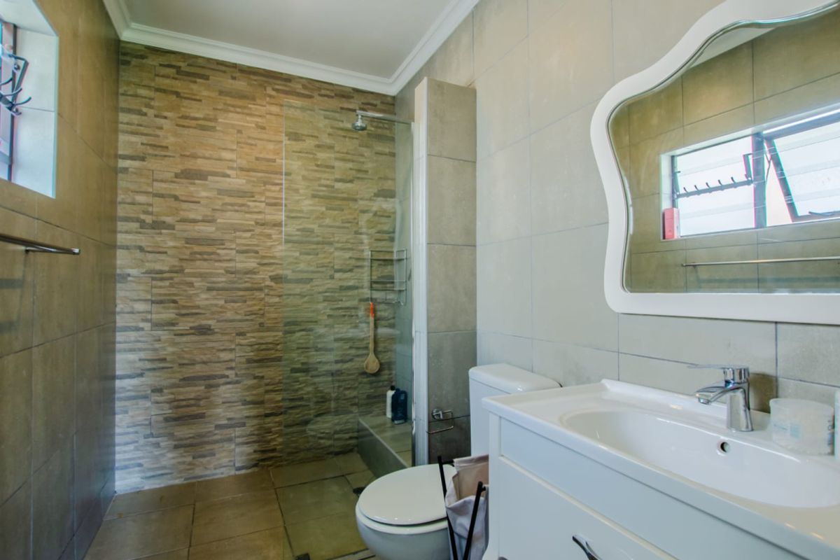 Modern bathroom featuring a glass-enclosed walk-in shower, textured stone-look feature wall, vanity basin, and neutral floor-to-ceiling tiling.