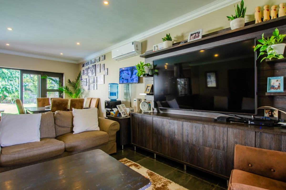 A comfortable living room featuring recessed ceiling lighting, a wall-mounted air conditioning unit, and large sliding glass doors providing access to the garden.
