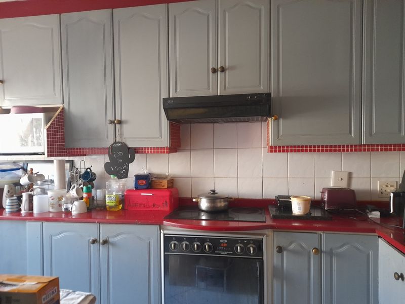 A functional kitchen featuring grey built-in cabinetry, a red countertop, and a built-in electric oven with an extractor fan.